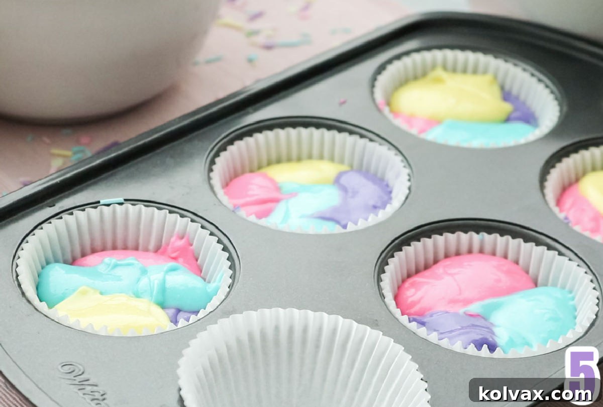 A closeup of a cupcake pan with liners, each filled with multi-colored cupcake batter layered to create a distinct marble effect before baking.
