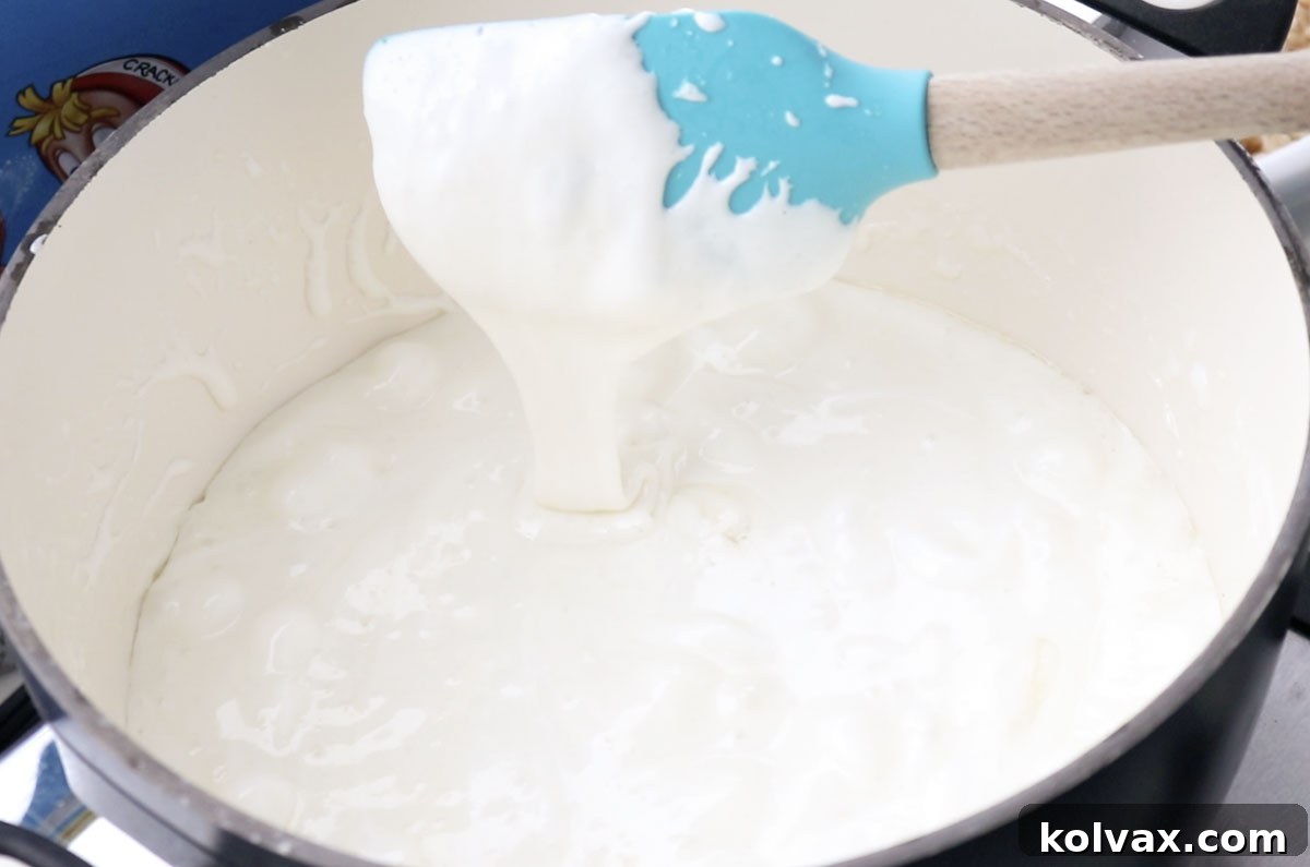 A medium-sized saucepan on a stovetop, filled with a bubbling, melted marshmallow mixture, ready to be combined with cereal.