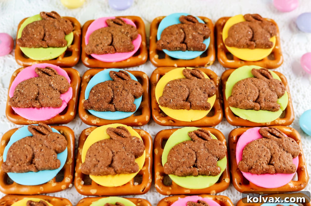 Three rows of pastel colored Chocolate Bunny Pretzel Bites laying on a white surface surrounded by Easter colored candies.