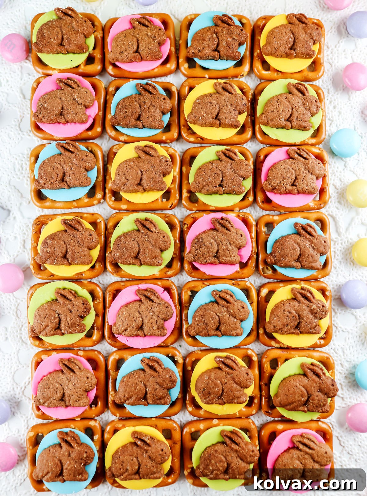 Closeup on rows of colorful Chocolate Bunny Pretzel Bites laying on a white surface surrounded by pastel colored candy.