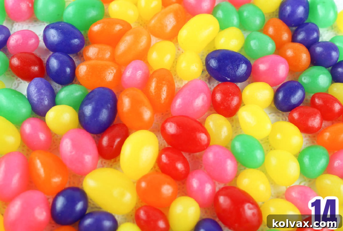 A large, vibrant pile of assorted jelly beans scattered enticingly on a crisp white table linen, with a handful of festive sprinkles nearby, all ready to be mixed into the warm popcorn.